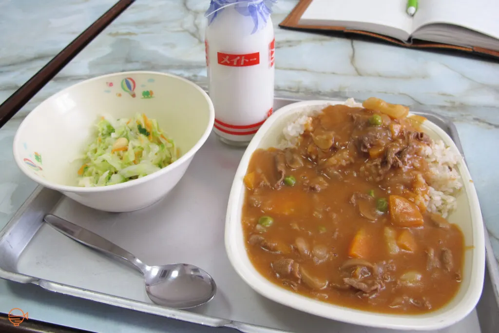 A beef and vegetable curry with rice and a pickled side salad, along with a bottle of milk.