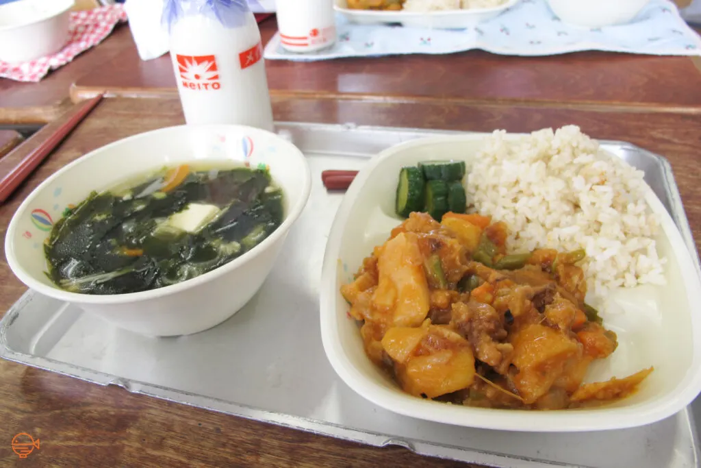 Sweet and sour pork with vegetables, rice and pickles, along with a bottle of milk.