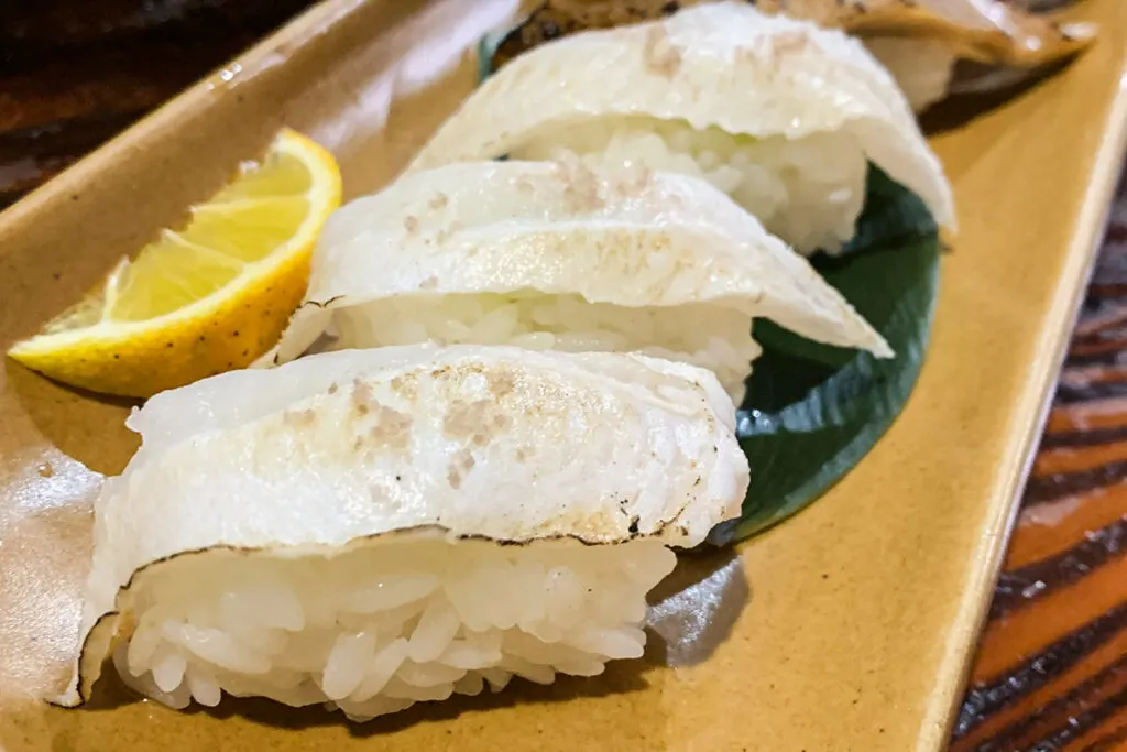 A serving of anago eel sushi, one of Tsushima Island's most famous foods, on a plate with a lemon wedge.