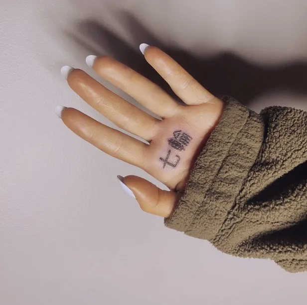 A photo posted to Ariana Grande's Instagram that shows her left palm facing the camera with the sleeve of her brown sweater covering the bottom part of her hand and a tattoo of two Japanese characters that say 'shichirin' (meaning a Japanese BBQ grill) at the top of her palm under her index and middle fingers.