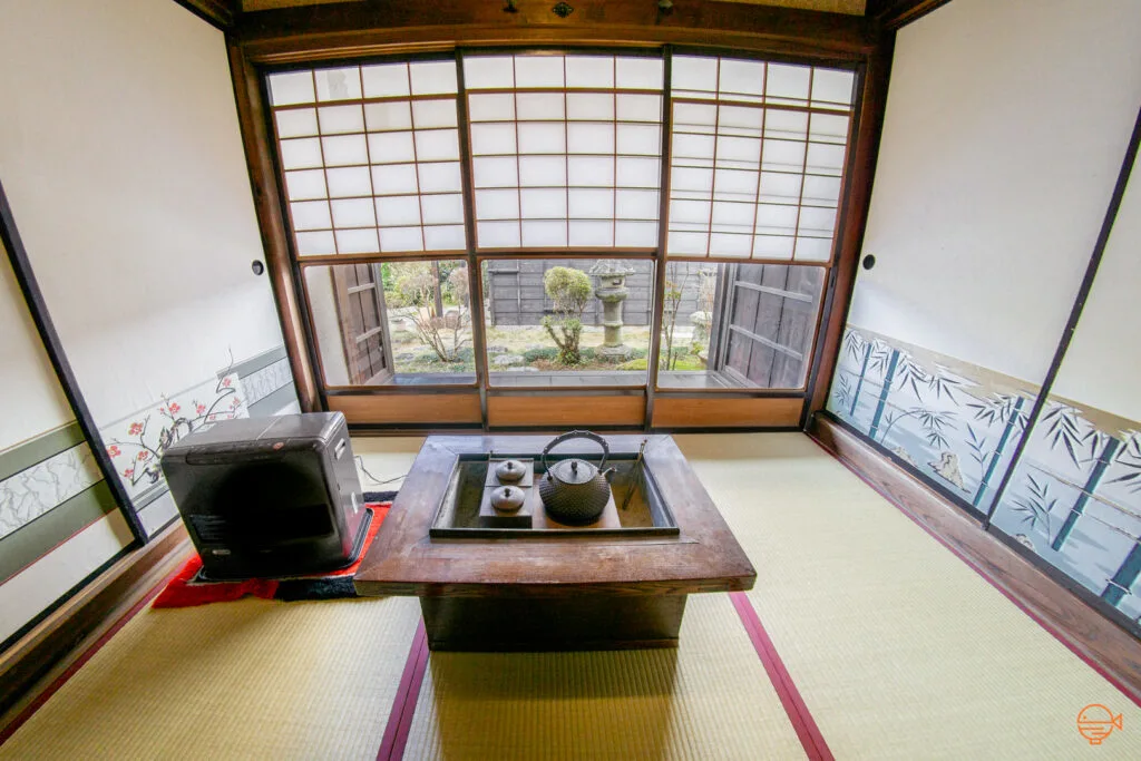 A hibachi sits in the middle of a traditional Japanese tatami room with a teapot and metal tongs inside the inner chamber.