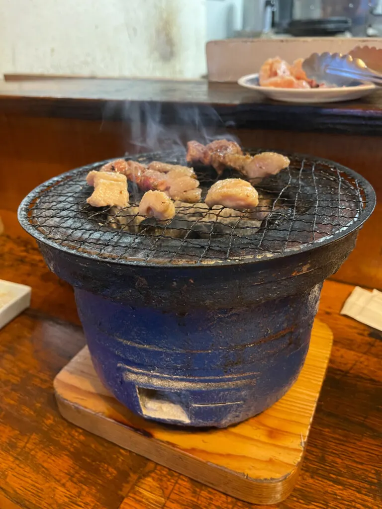 A clay pot with charcoal inside and meat cooking on the metal grill placed on top (this type of Japanese grill is known as a shichirin in Japanese). Photo by Saki Inoue.