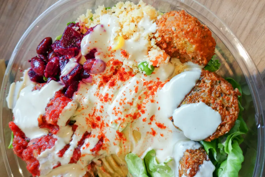 A close up shot of a falafel salad bowl with various colorful salad items (including beetroot, corn, lettuce and pickles), falafel and hummus. Photo by author, Kaori S.