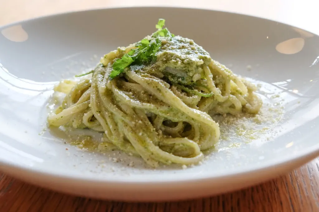 A serving of pesto spaghetti on a large white lipped plate. Photo by author, Kaori S.