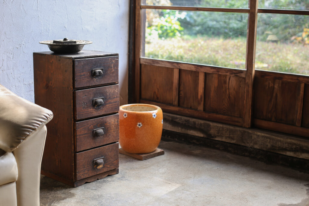 An orange-colored hibachi pot sits on the floor next to a chest of drawers in the corner of a traditional Japanese room. 