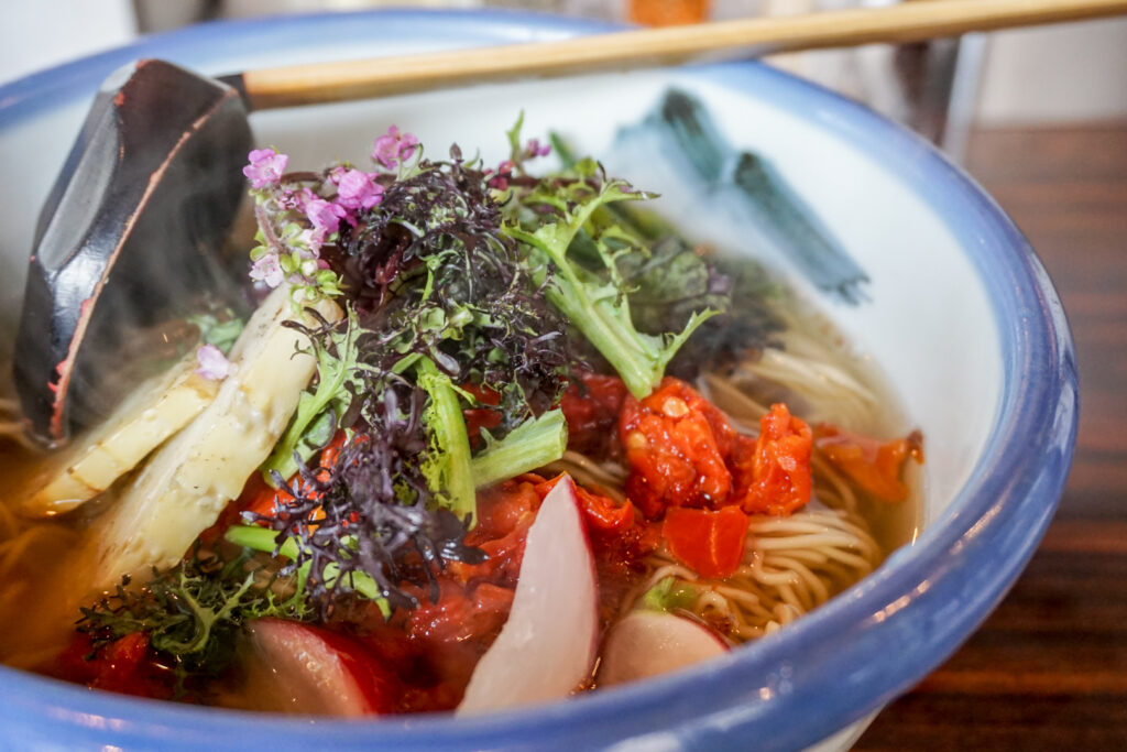 A colorful bowl of Afuri's Rainbow Vegan Ramen in Tokyo. Various green, red, white and purple vegetables top the ramen noodles and soup in a white ceramic bowl with a blue lip.