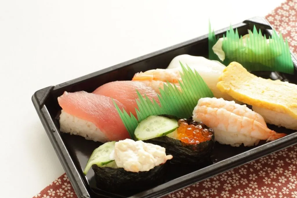 A sushi bento with sushi grass separating the two rows of sushi items and also the pickles.