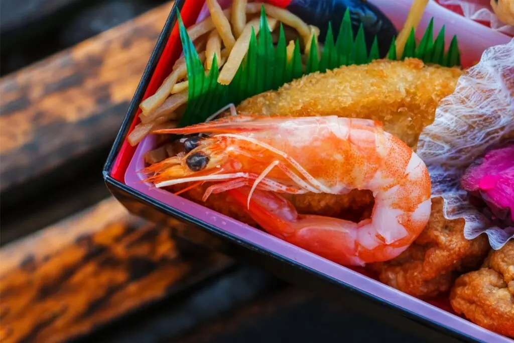 A corner of a bento box can be seen with sushi grass separating the meat and vegetable items. Via Getty Images.