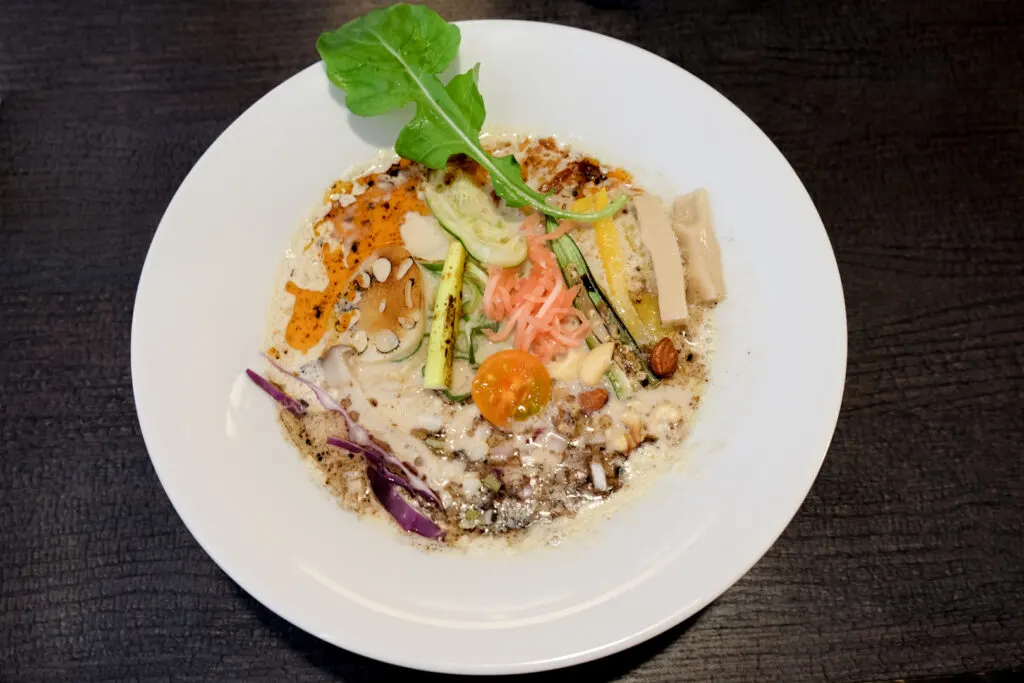 Vegan Paitan ramen from Cinq in Chigasaki with its thick and creamy mushroom-colored soup and plenty of vegetables, served in a shallow white bowl that looks more like a plate.