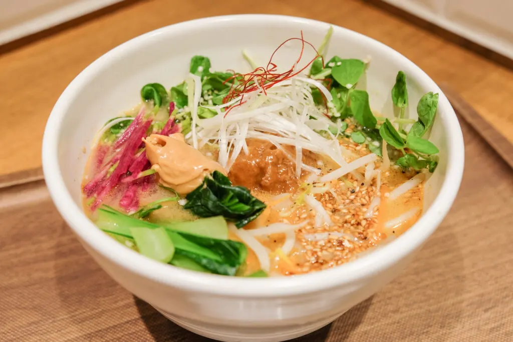 A bowl of T's Tan Tan Golden Sesame Vegan Tantanmen - with its golden broth, and pops of green, red and white veggies.