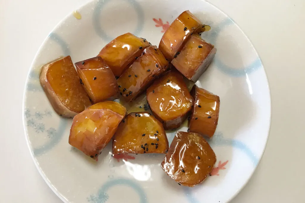 A white plate with a light blue ring pattern on it. On the plate is sweet potato fried in oil and covered in honey.