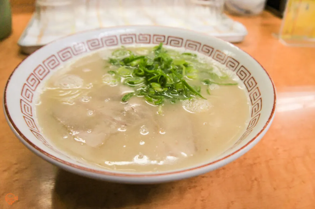 A bowl of tonkotsu ramen (pork bone broth) with chashu pork slices and spring onions on top.