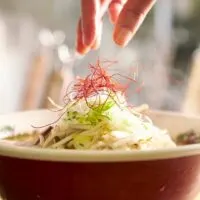 A hand can be seen gently adding saffron to the top of a steaming bowl of miso ramen.