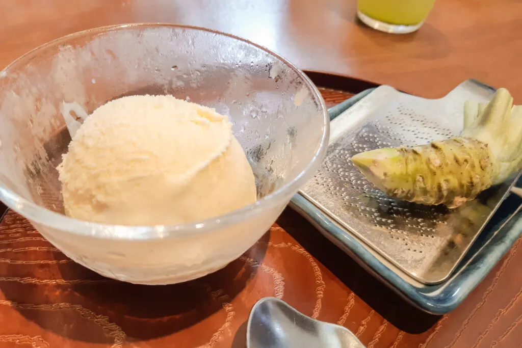 To the left of frame is a chilled glass bowl of vanilla ice cream, and to the right is a wasabi rhizome (thickened stem) on top of a metal grater ready to be grated by the customer and enjoyed with the ice cream.