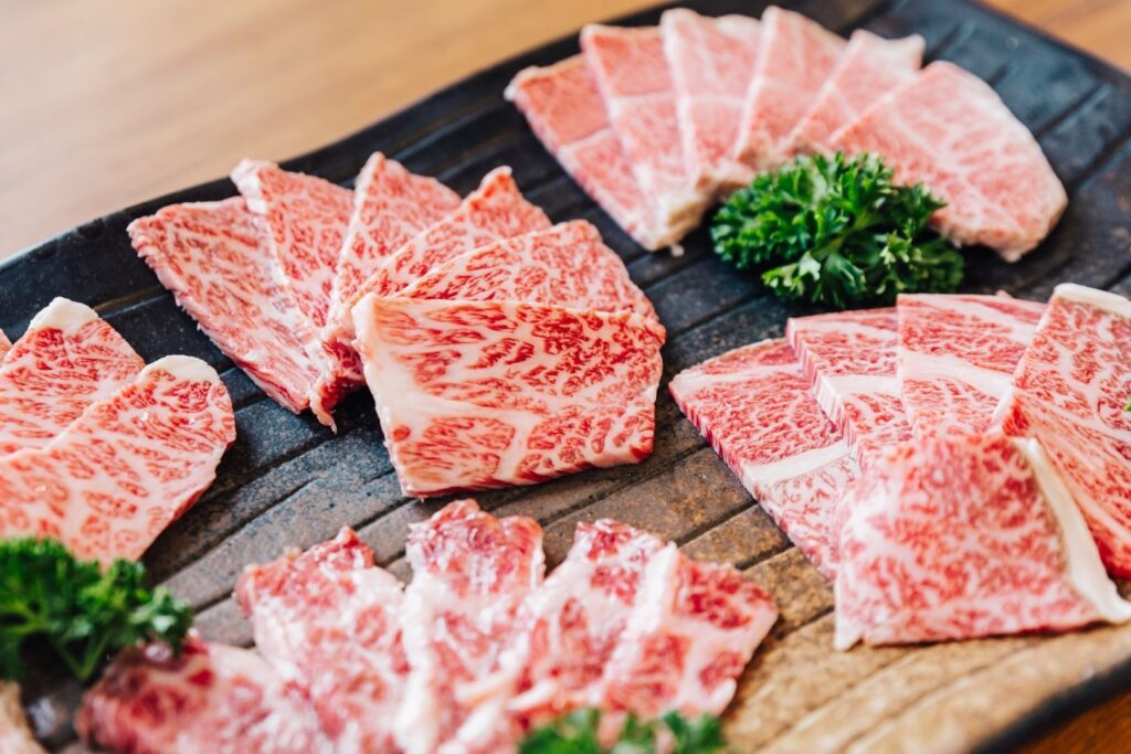 A variety of slices of raw a5 wagyu are arranged on a large plate with parsley as a garnish.