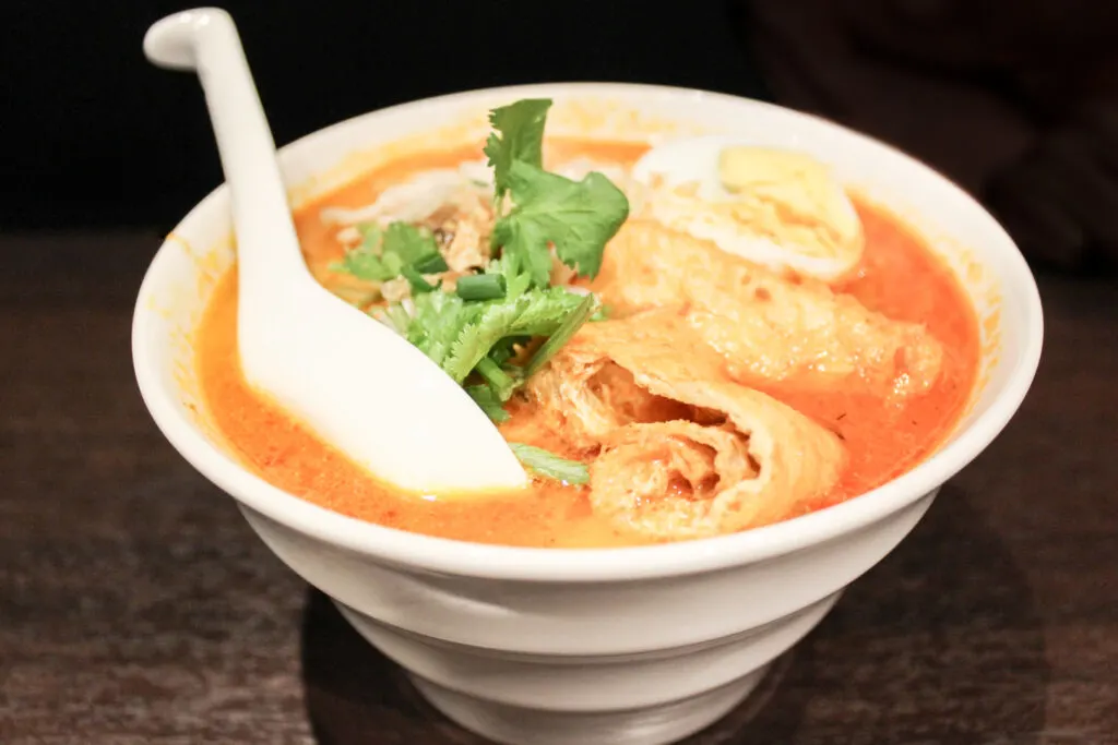 Halal restaurants in Tokyo - a bowl of spicy, orange-colored mi kari with a white spoon in it at Malay Asian Cuisine.