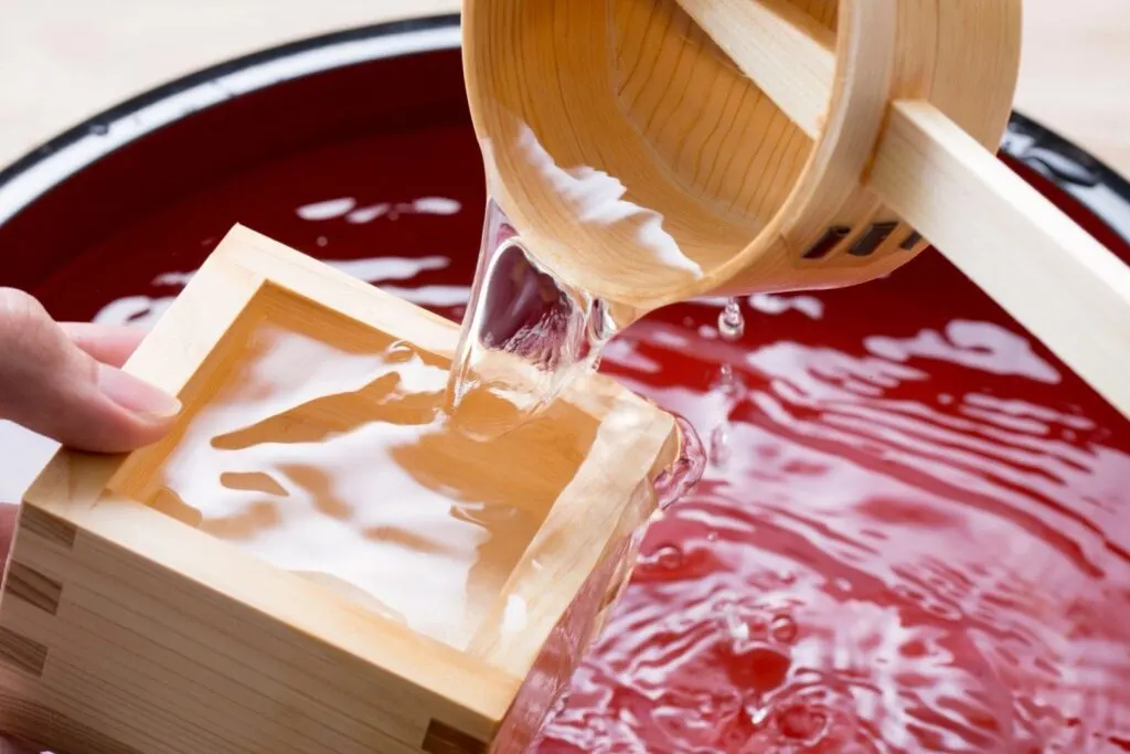 Drinking sake in a box: A wooden ladle is being used to abundantly pour sake from a barrel into a wooden masu cup.