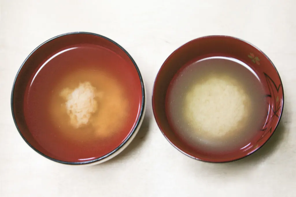 Two bowls of miso soup side-by-side. The broth has separated from the miso paste and the miso has gathered in the middle of each bowl like a ball. The bowl to the right has a rounder "ball," while the one on the left has more miso at the base and a smaller amount at the top.