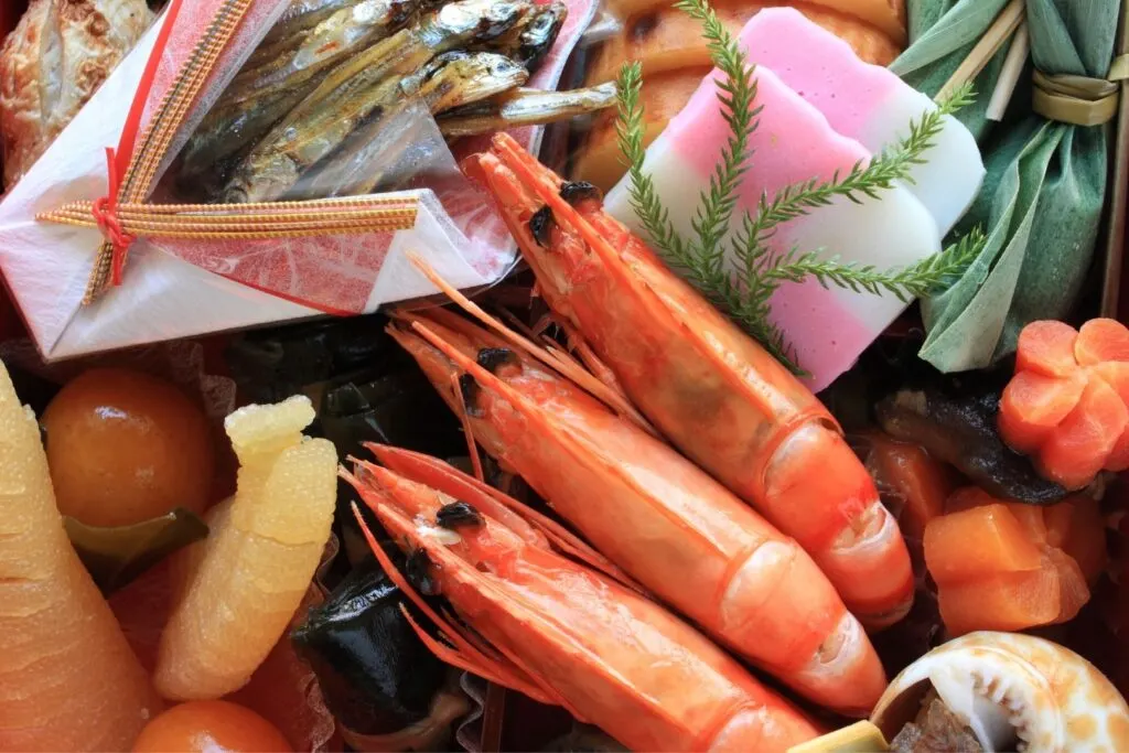 An overheard shot of an osechi box with three shrimp as the focal point.