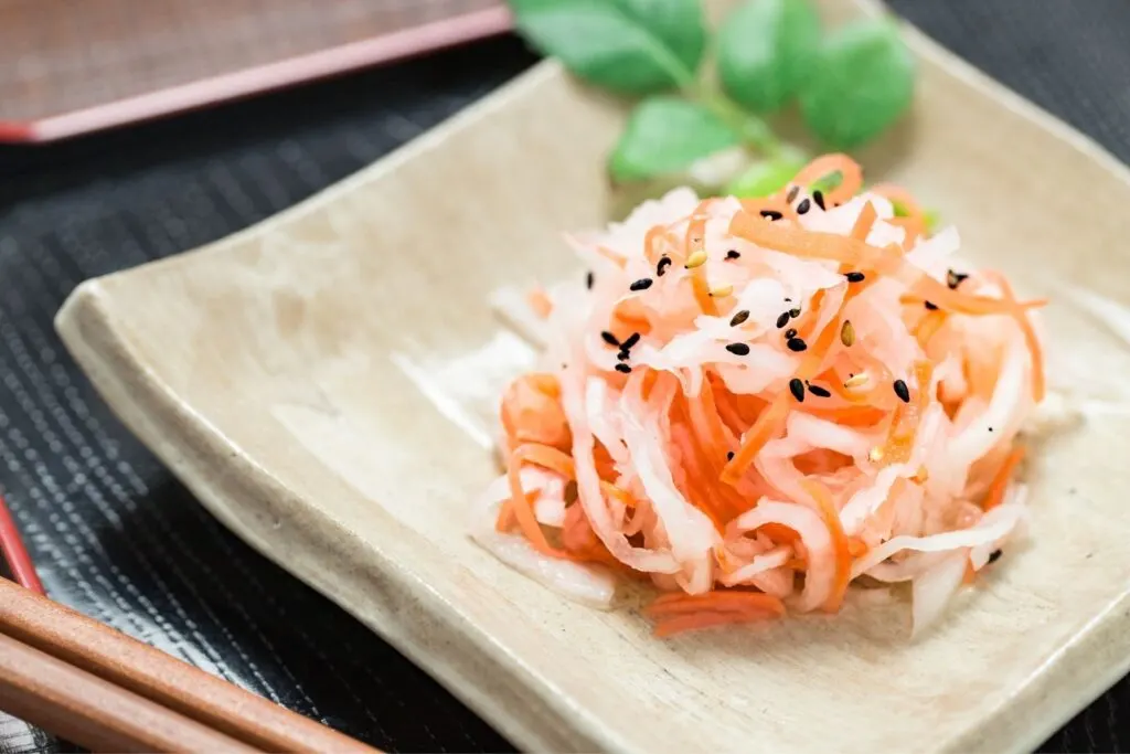 A serving of kohaku namasu on a beige ceramic dish with some black and white sesame seeds sprinkled on top.