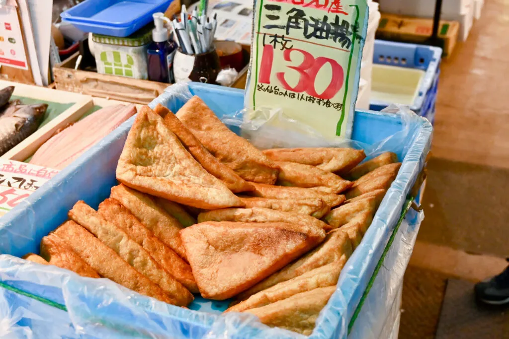 A blue plastic box of triangle-shaped deep-fried tofu (sankaku abura-age) for sale at a local market.