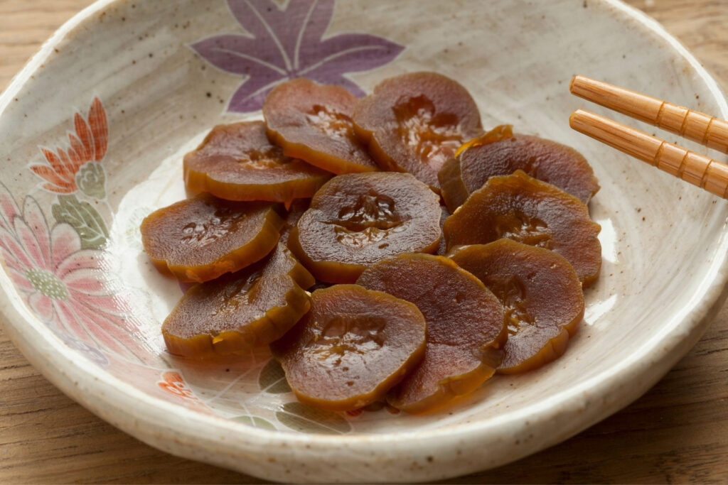 A plate of brown narazuke pickles arranged in a flower design on a beige ceramic plate with a colorful flower pattern on half of the rim. Wooden chopsticks can be seen coming in from the right of the image.