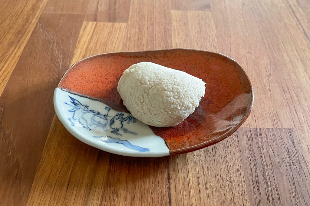 A handful-sized portion of kneaded nerikasu paste on a red and white ceramic plate with a blue frog and rabbit design on the white part, sits on a wooden surface.