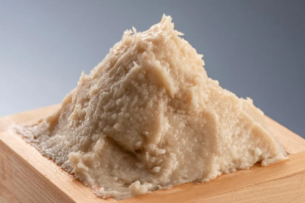 A wooden masu cup filled with a light-brown sake kasu paste that has been formed into a peak.