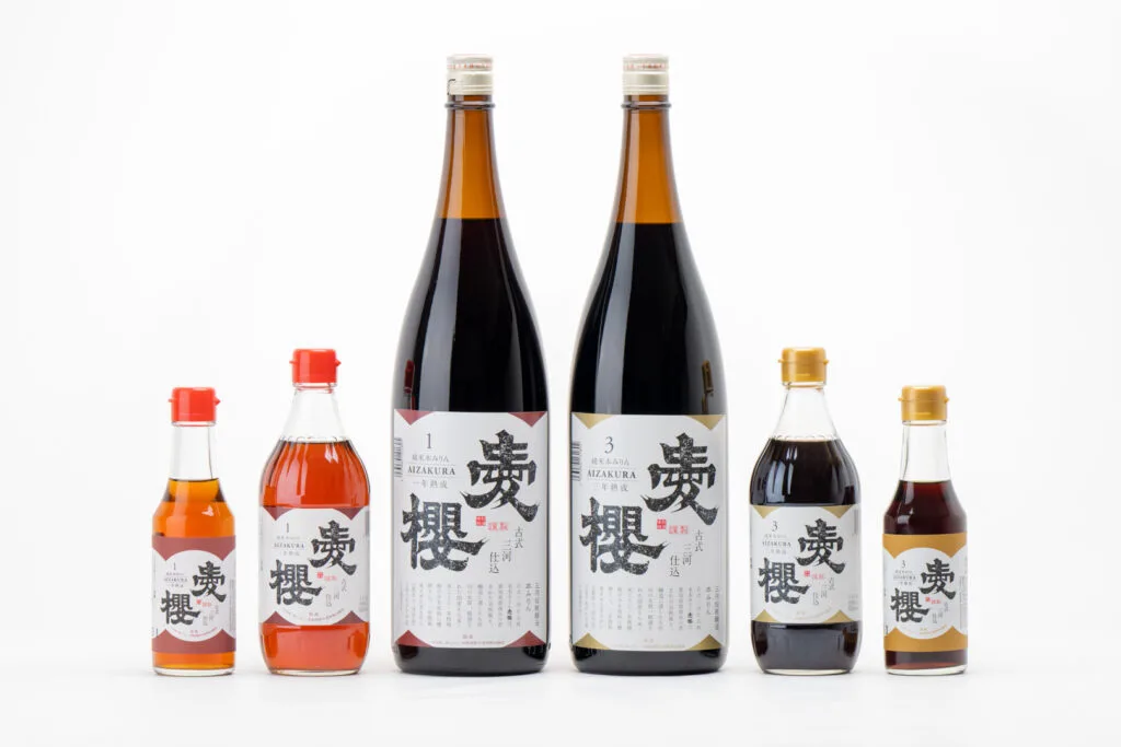 Six bottles of Hon Mirin. The two in the middle are the largest, then two medium-sized bottles are on either side of those, and then two smaller bottles next to them, creating a triangle/pyramid shape. The first three in the row have been aged for one year and the second three have been aged for three years.