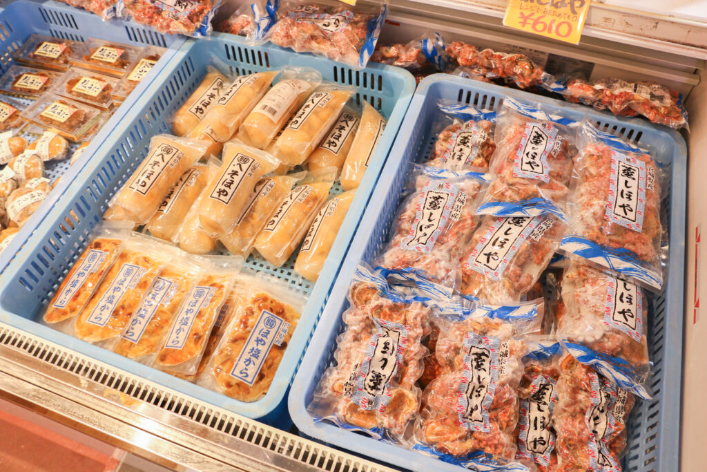 Plastic-wrapped sea squirt and sea urchin products on display in shallow blue plastic baskets at Katakura Shoten.
