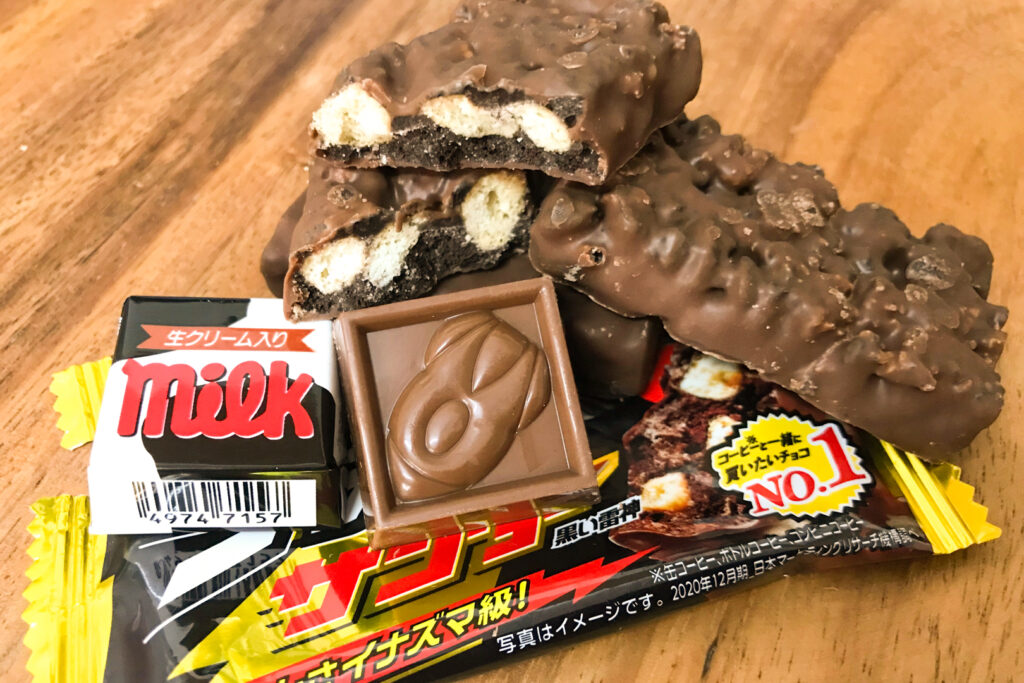 Black Thunder and Tirol Choco packaging with some unpackaged chocolate bars/pieces arranged on top, on a natural-colored wooden surface.