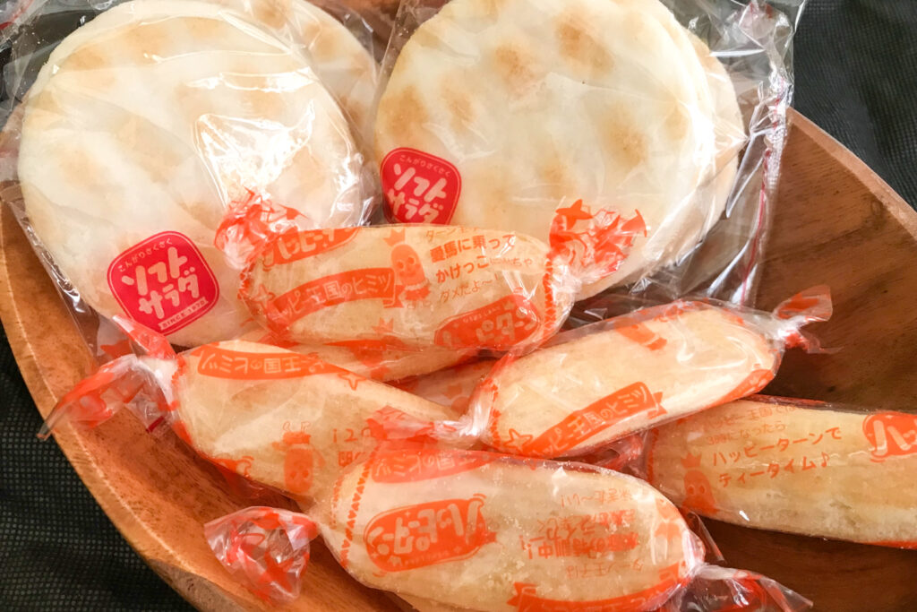 Popular Japanese snacks: A wooden bowl filled with some large round 'Soft Salad' rice crackers at the back and smaller oval-shaped 'Happy Turn' rice crackers at the front.