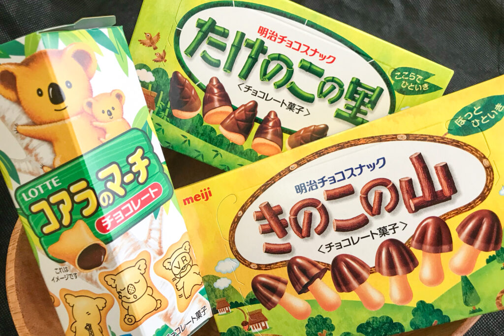 Japanese snacks: A box each of Koala March, Takenoko no Sato and Kinoko no Yama arranged in a wooden bowl.