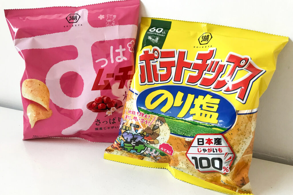 Two packets of Japanese chips: A pink packet of ume (plum) flavor and a yellow packet of nori-shio (seaweed salt). Both sit side by side on a white surface, leaning up against a white wall.