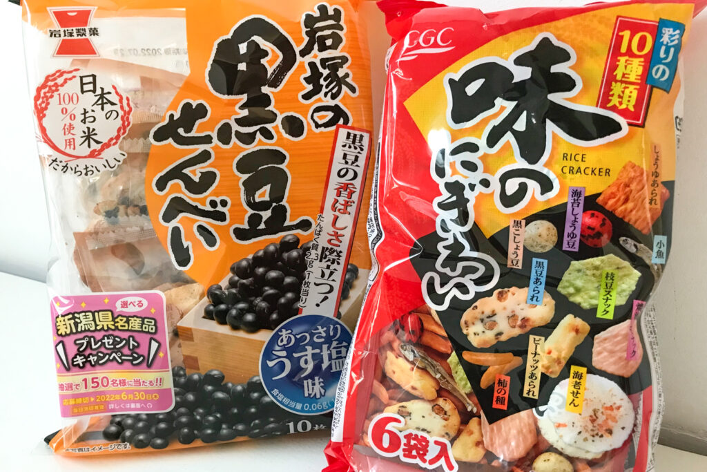 Popular Japanese snacks: Two packets of more unusually-flavored senbei rice crackers sitting side by side on a white surface leaning up against a white wall.