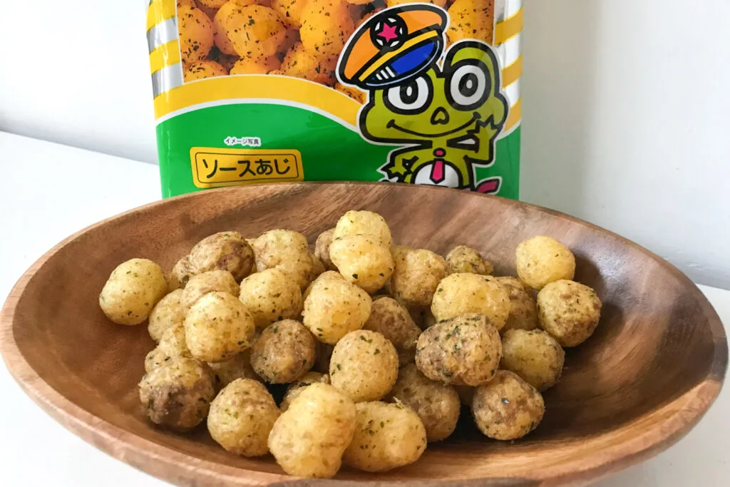 A wooden bowl filled with round balls of kyabetsu taro corn puffs. Behind it part of the plastic packaging with a frog on it can be seen.