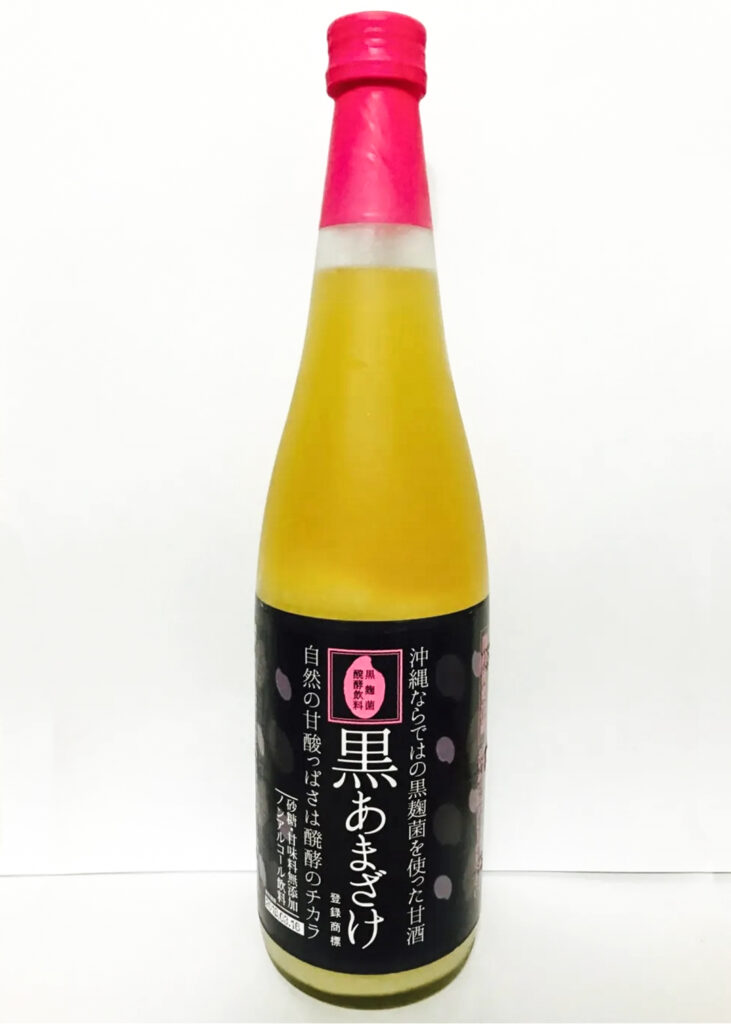 A bottle of Kuroamazake ('black amazake' derived from black koji). The bottle cap is red and the label is black with white writing. The liquid can be seen through the clear bottle and is a golden yellow color.