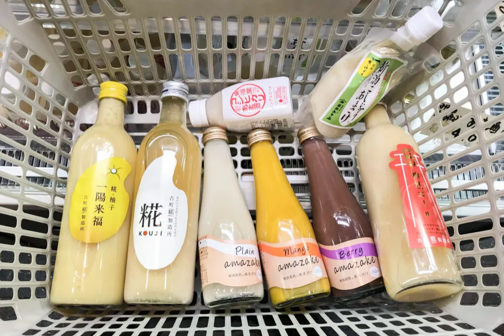 A shopping basket filled with a selection of amazake products, including mango and berry flavored versions.