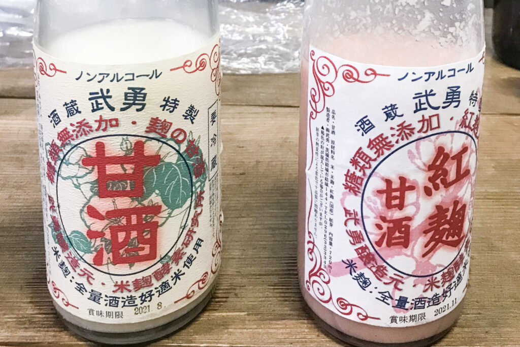 Two glass bottles on a table - Regular yellow koji amazake on the left (which produces a white product) and red koji (monascus) amazake on the right (which produces a pink product).