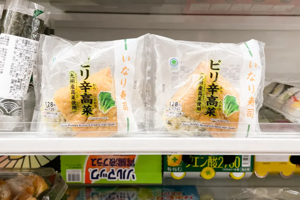 A spicy pickled mustard green (takana) version of inari sushi on a Japanese convenience store shelf.