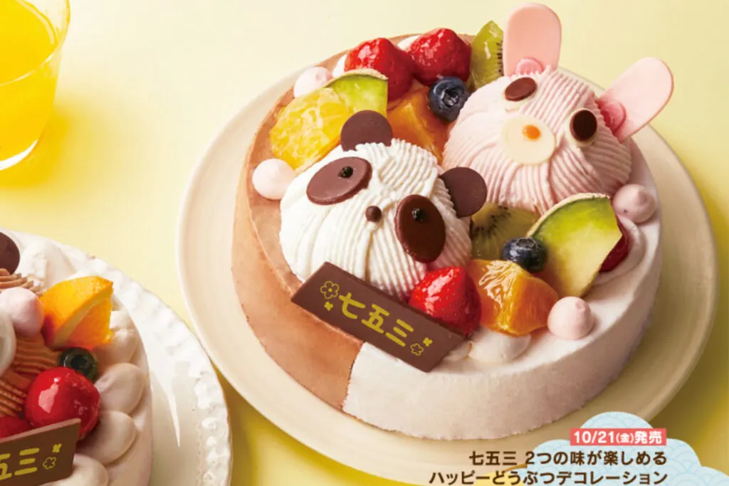 A Japanese Shichi go san cake decorated with a panda and a rabbit (rounded pieces of cake added to the top and frosted to give a 3D effect), along with various cut fruits and a chocolate plaque that reads 'Shichi go san' in kanji (七五三).