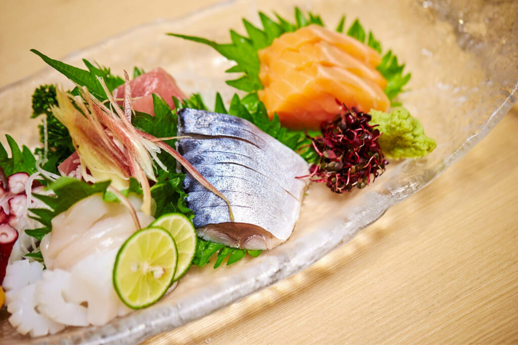 Raw fish and seafood on a plate of daikon radish strings and shiso leaves, and various other sashimi garnishes including myoga Japanese ginger on top.