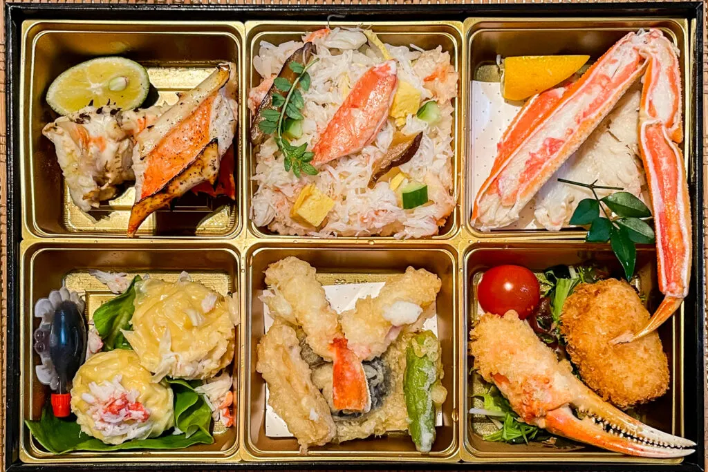 A six compartment kani bento (crab lunch/meal box) with crab prepared various ways from Kani Doraku crab restaurant on Dotonbori in Osaka. The crab shumai dumplings even have a little soy sauce bottle, the kind you'd typically get with takeout sushi, in the shape of a crab.