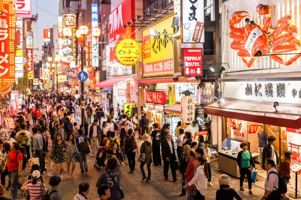 A night time shot of a bustling Dotonbori, Osaka. To the right, the giant orange mechanical moving crab above Kani Doraku restaurant can be seen.