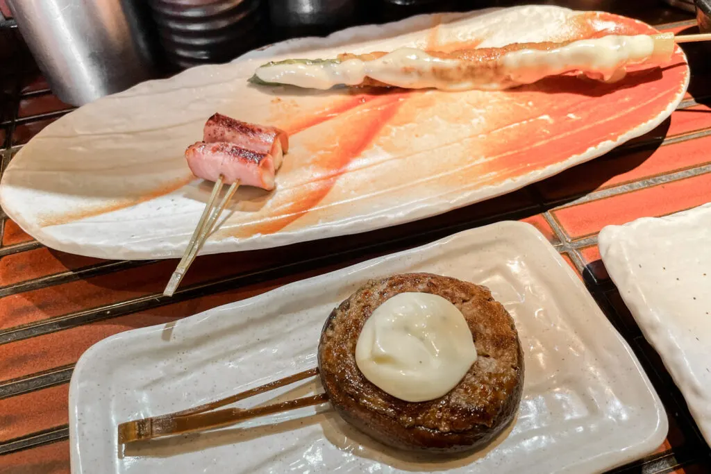 Kushikatsu (battered and fried meat and vegetables on skewers) at Teppanjinjya teppanyaki restaurant on Dotonbori, Osaka. Clockwise from the top right: Asparagus in mayonnaise, shiitake mushroom with minced meat and bacon-wrapped camembert cheese.