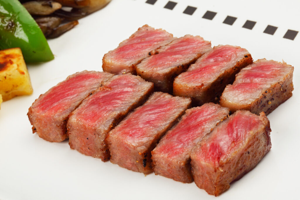 Miyazaki food: A large white plate with nine perfectly-seared pieces of Miyazaki beef (Miyazaki-gyu) cut to show their rare to medium rare insides. Some vegetables are slightly in view to the left.