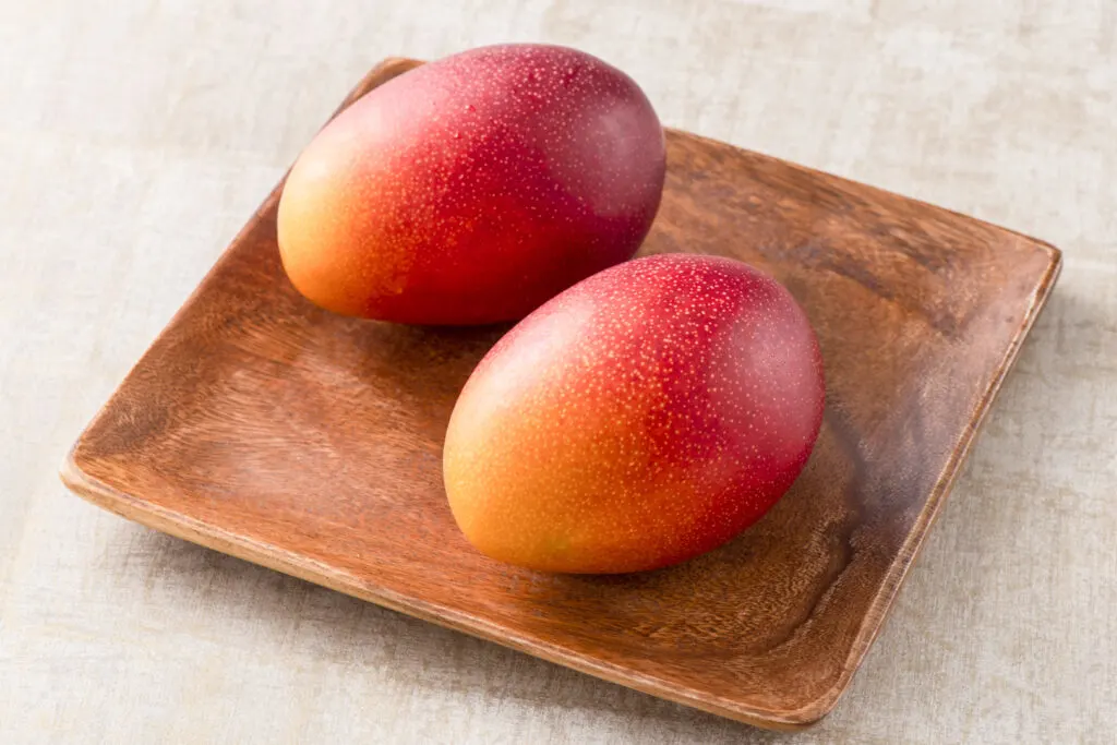 Miyazaki food: Two perfectly symmetrical Miyazaki mangoes sit on a wooden platter. The color fades from a dark red at one end to a peachy yellow at the other.