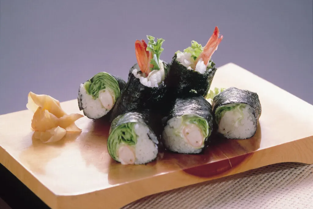 Miyazaki food: Six pieces of cut Lettuce Maki sit on a wooden chopping board with some pickled ginger. These sushi rolls contain lettuce, shrimp, mayonnaise, vinegared sushi rice and are rolled up in nori seaweed.