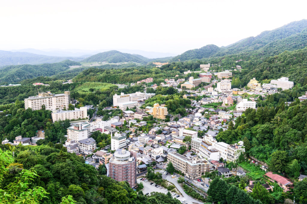 A picture of the Arima Onsen township from an elevated position during the daytime, showing the town surrounded by mountain greenery.