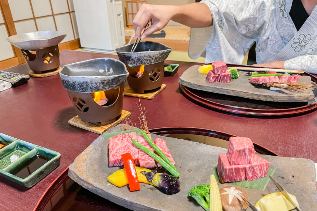 A table setting for two at a ryokan in Arima Onsen. There is raw Kobe beef and vegetables beautifully presented on large stone plates. The food is ready to be cooked on each person's individual cooking apparatus.